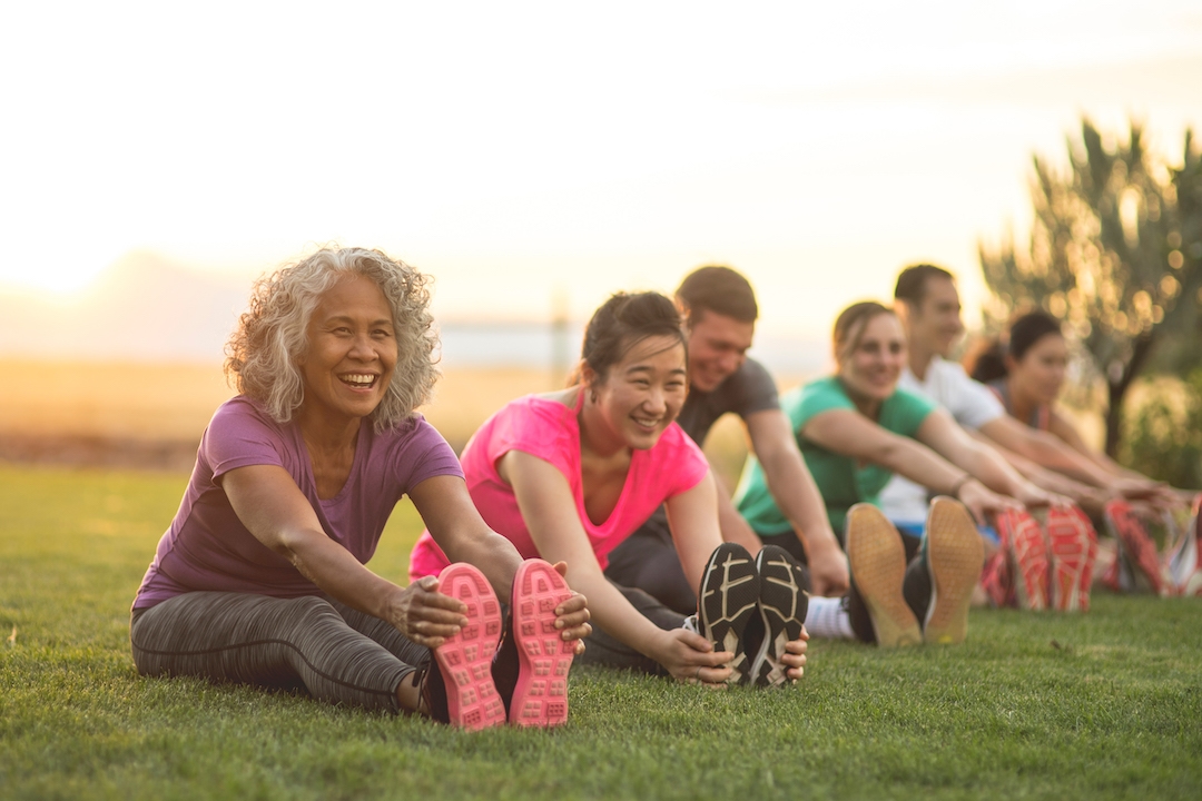 group photo of people sitting on the grass stretching touching their to