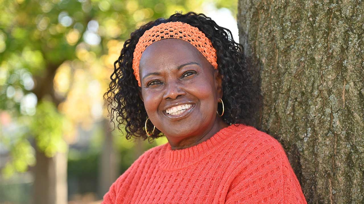 woman standing by a tree with an orange sweater and black hair